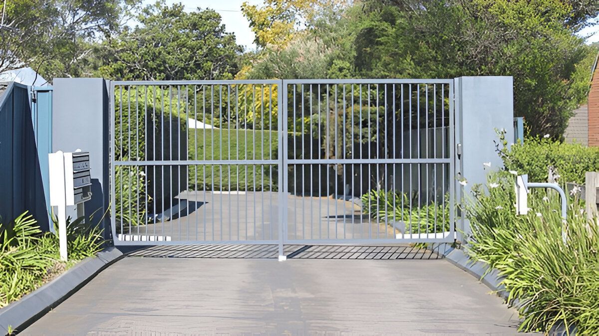 A metal gate is open to a driveway leading to a house.