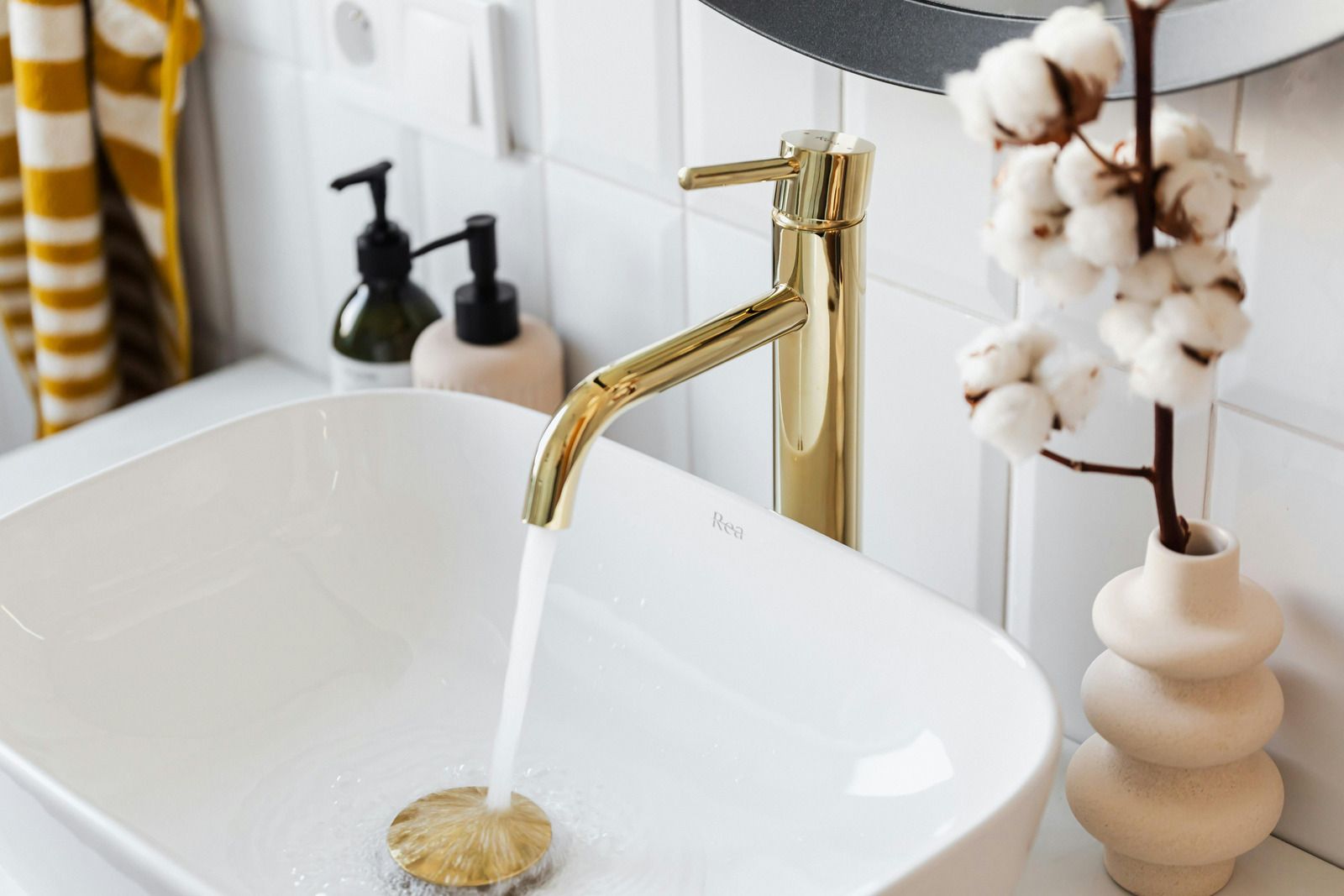 Gold faucet pouring water into a white sink in a modern bathroom.