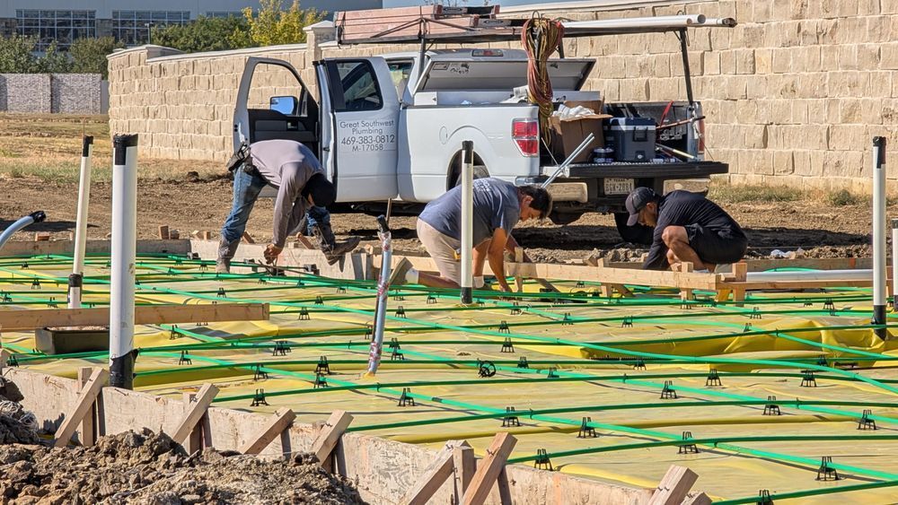Construction workers building a foundation, using wood frames and yellow/green mesh, by a white truck and retaining wall.