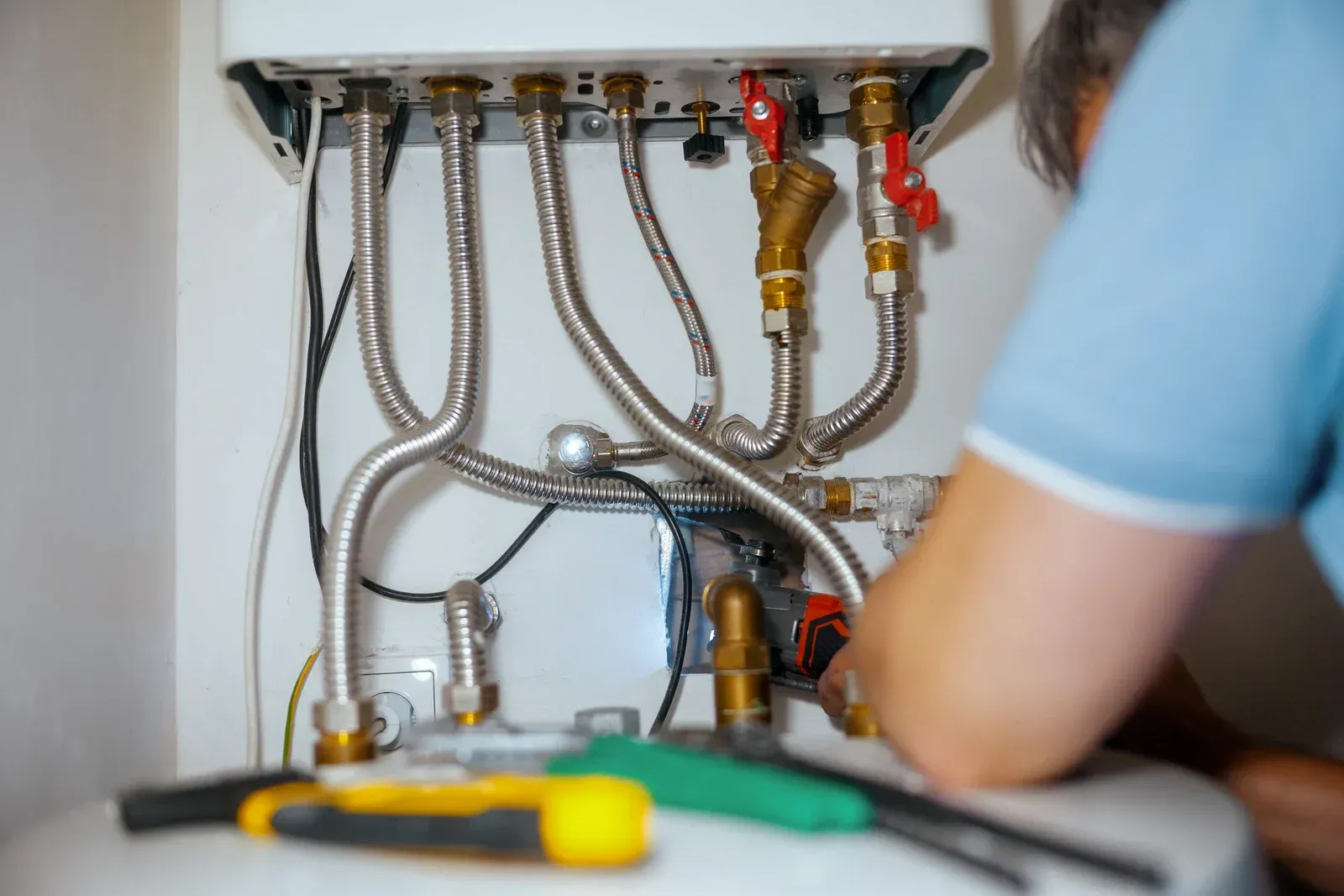 Person working on water heater pipes with tools.