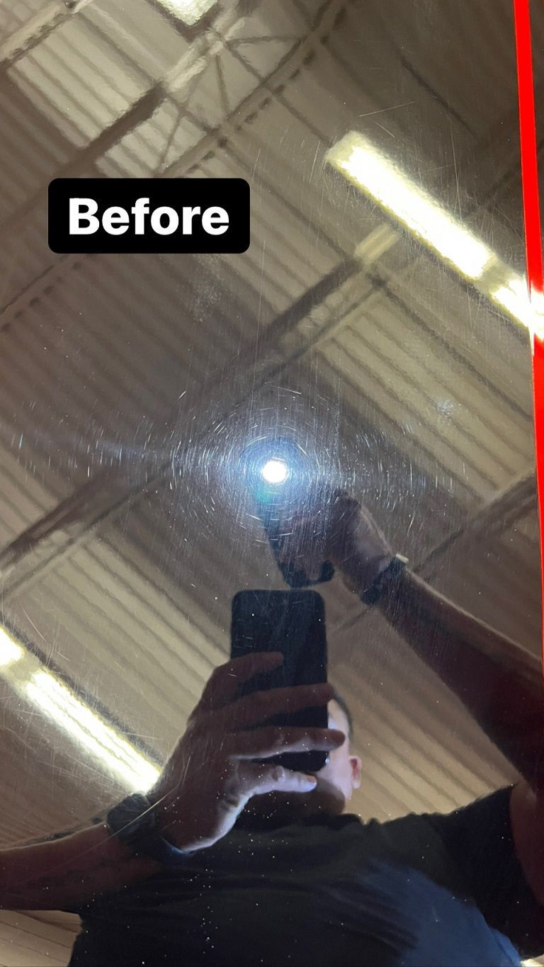 Black car surface before polishing, illuminated by a flashlight. Person holding phone reflects. 