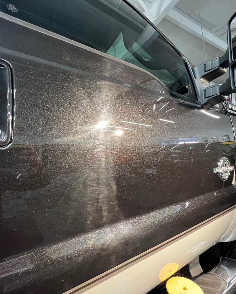 Close-up of a brown truck panel with swirl marks and paint imperfections visible under a light.