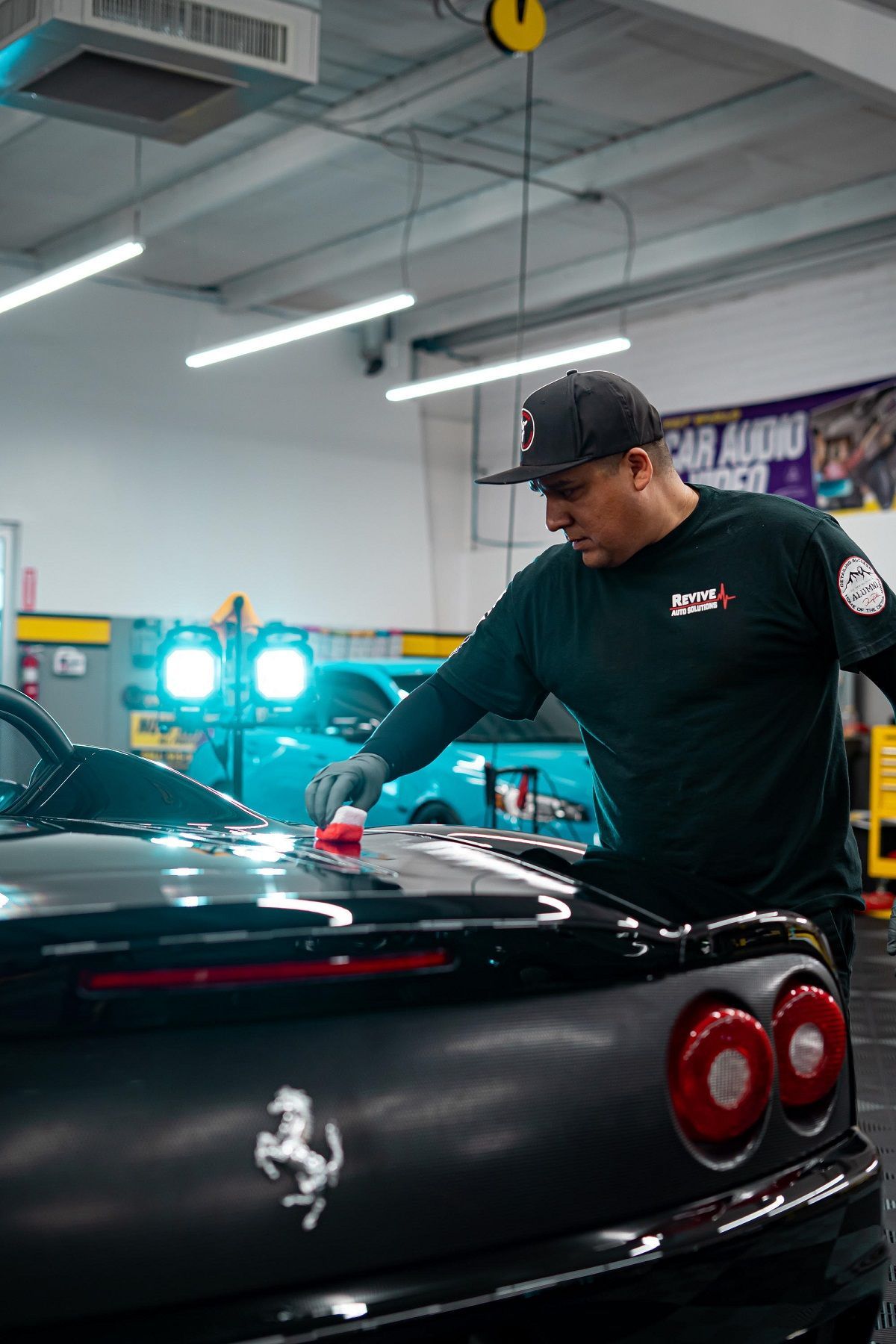Man applying product to a black Ferrari in a garage.