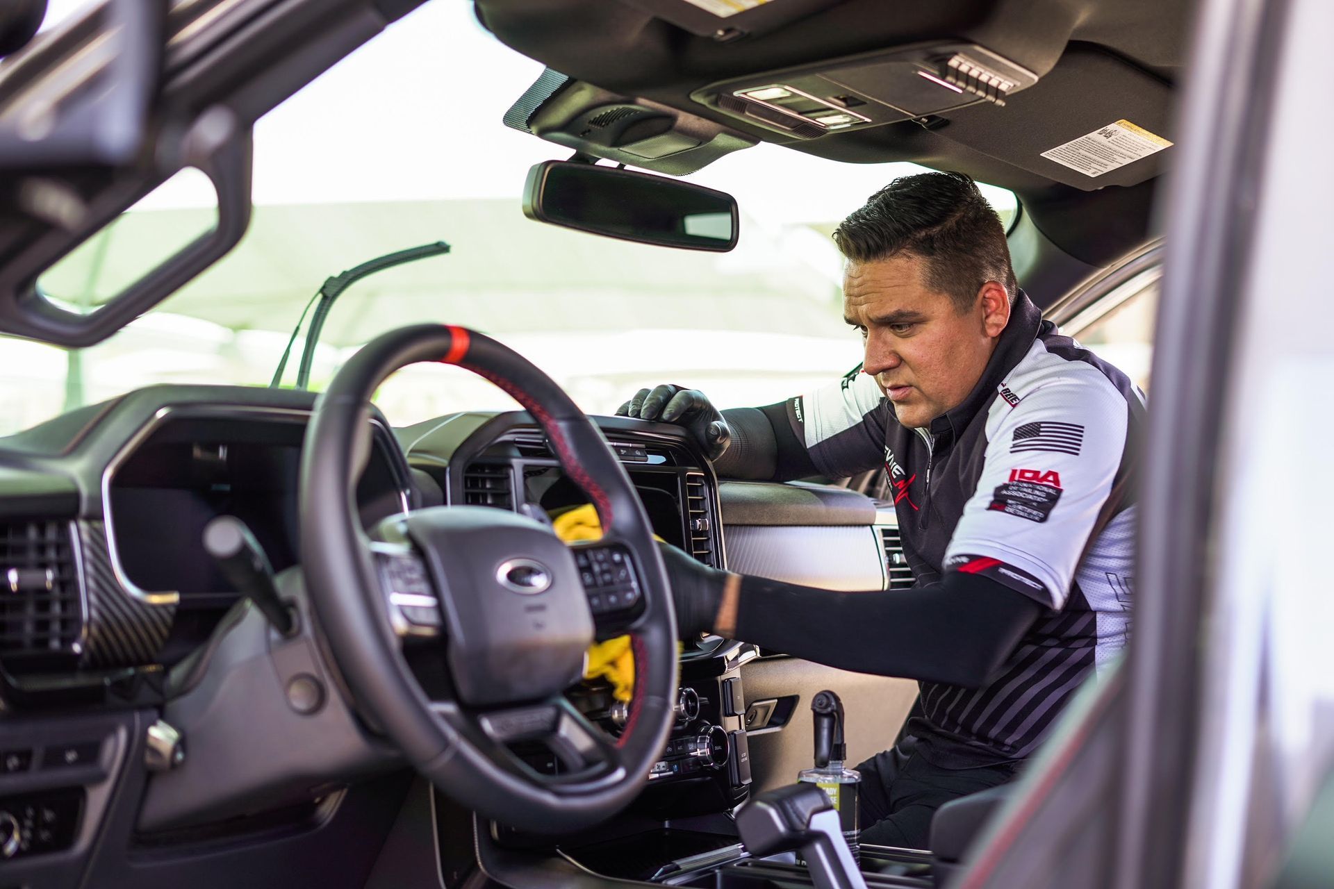 Mechanic cleaning the interior of a Ford truck; wiping dashboard with a cloth, black gloves.