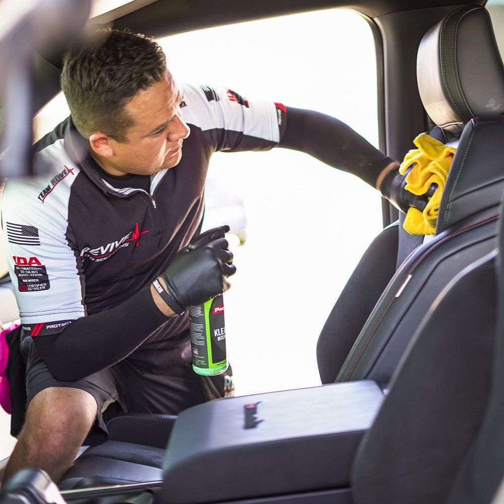 Man cleaning car interior with spray bottle and cloth.