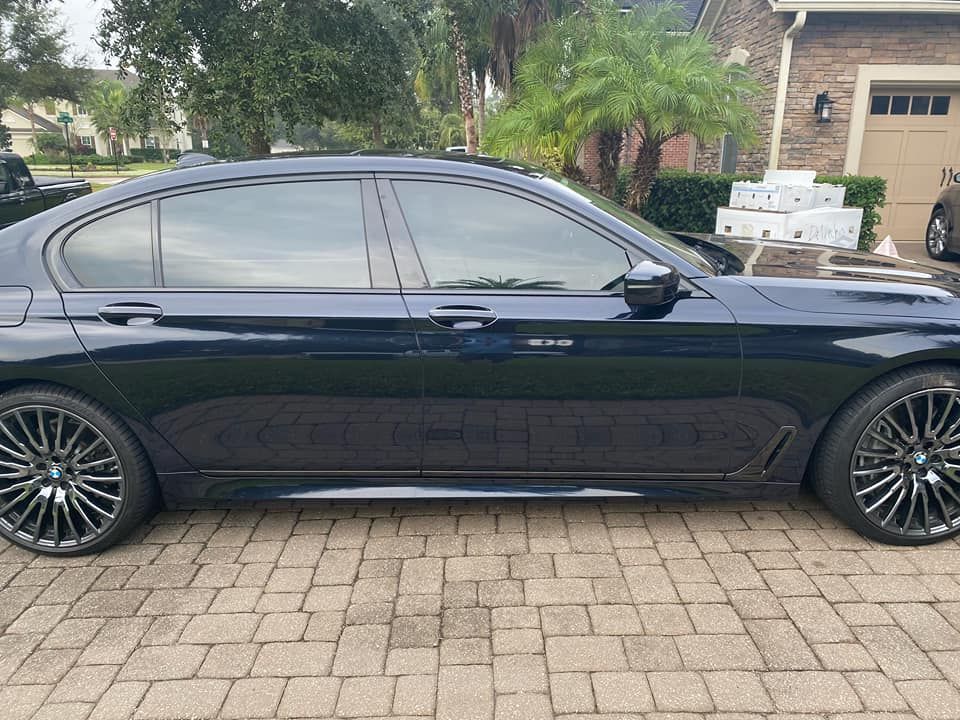A black car is parked on a brick driveway in front of a house.