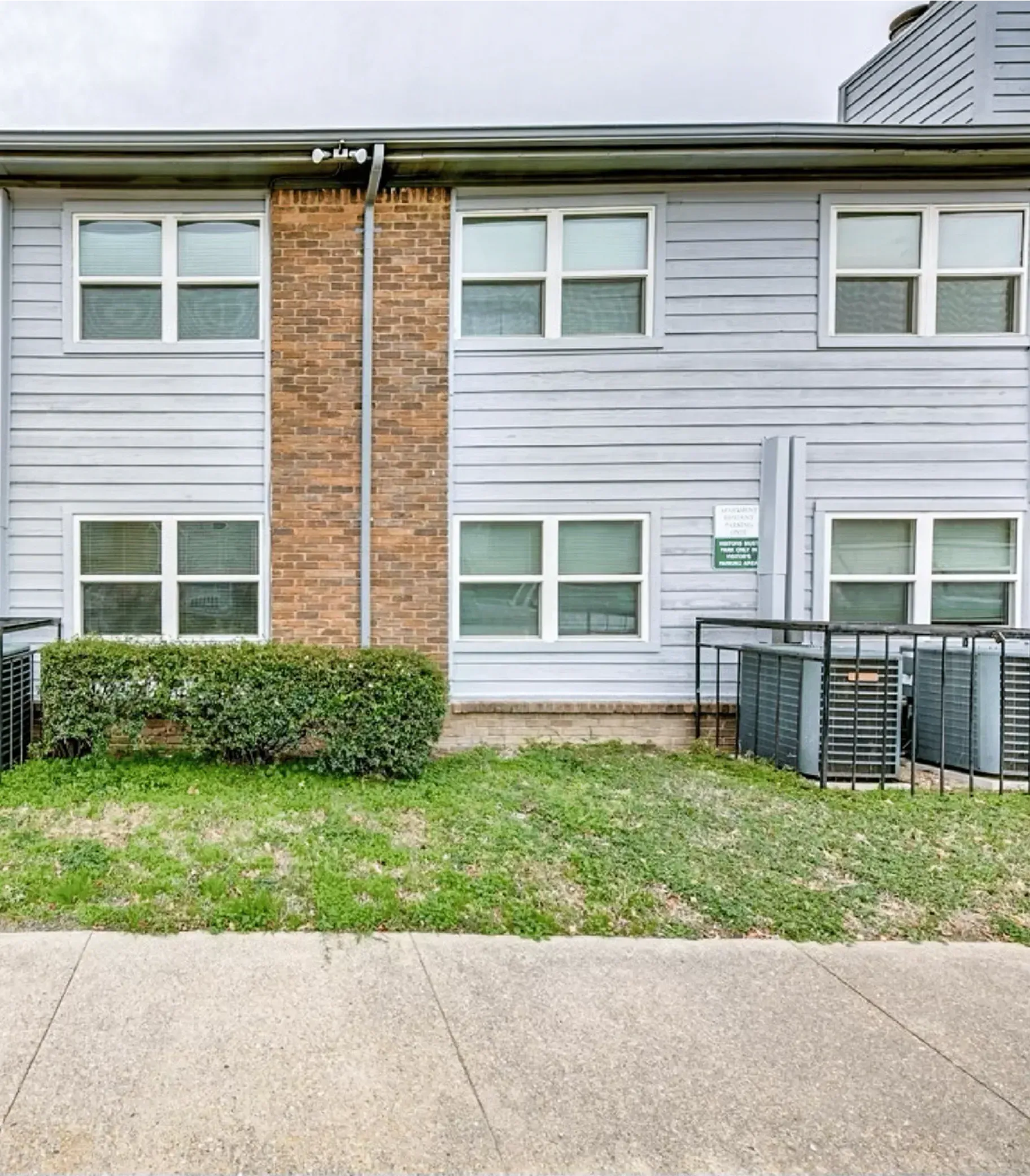 A white house with a brick wall and a lot of windows is for sale.