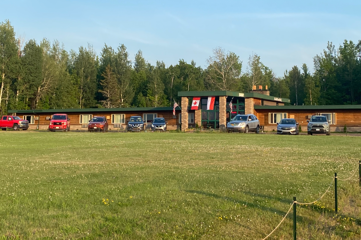 A row of cars are parked in front of a motel.