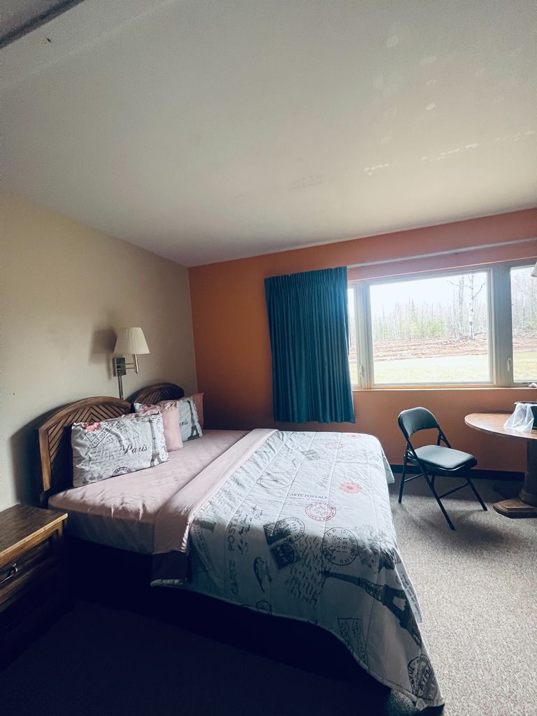 A hotel room with a king size bed , chair , table and window.
