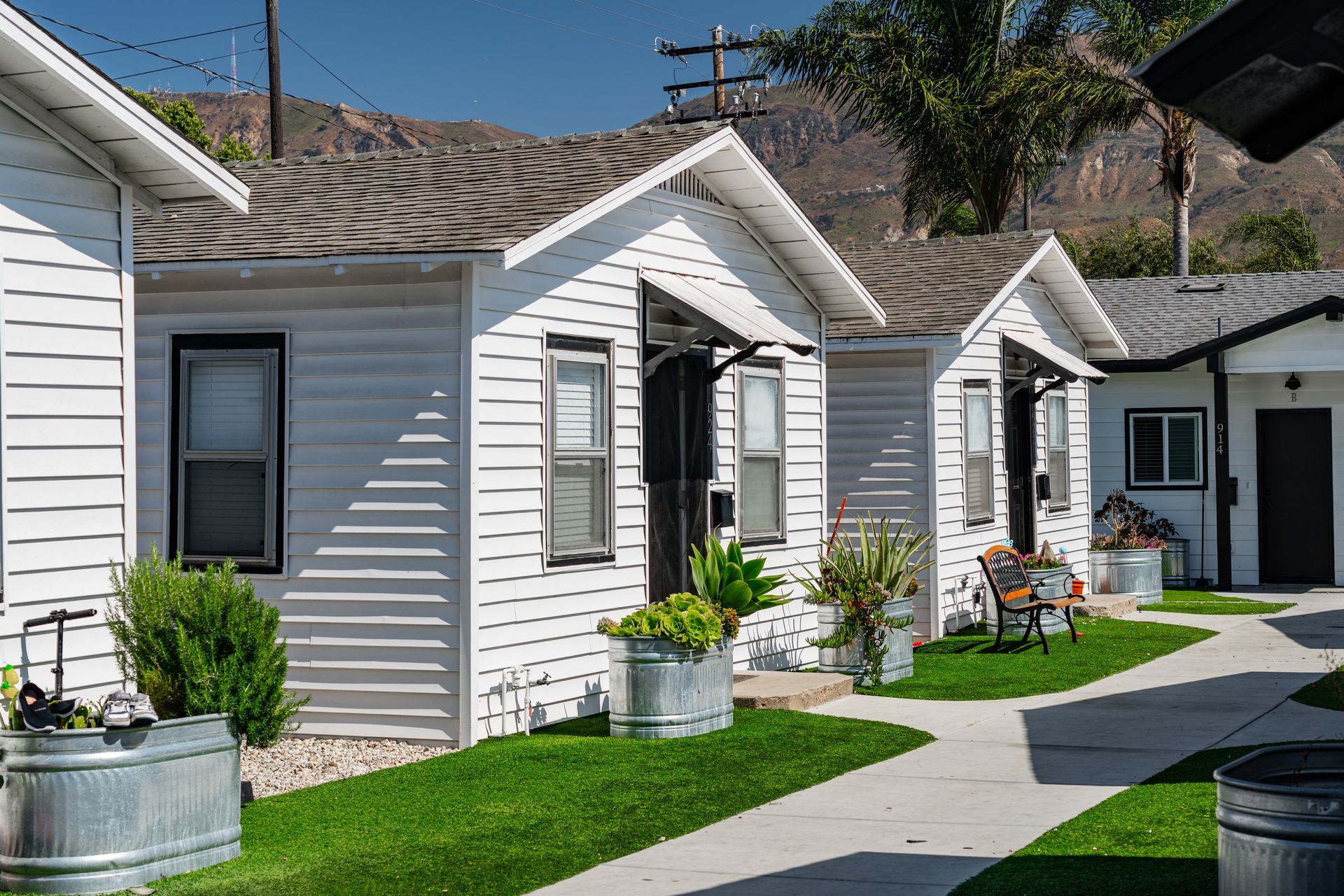 White cottages with black trim and metal planters along a walkway, mountains in the background.