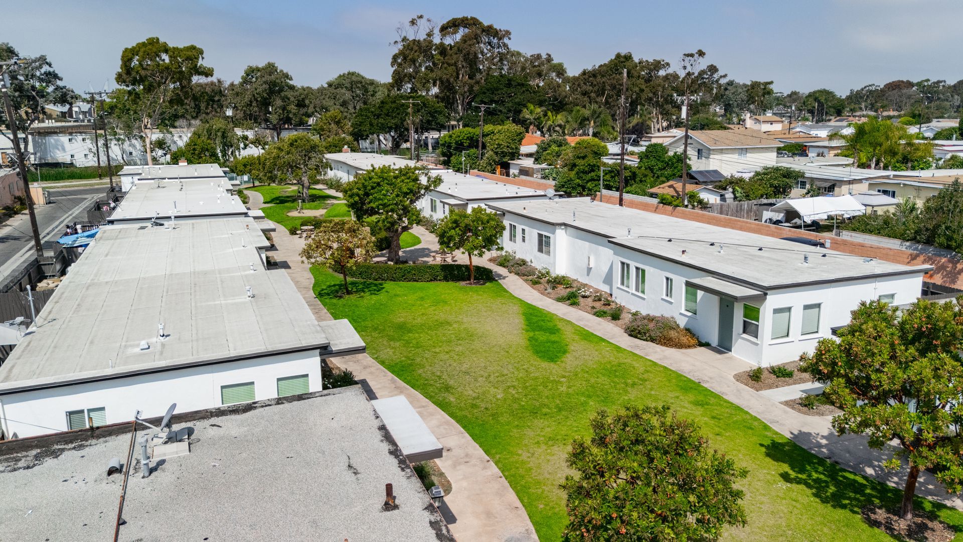 Aerial view of white buildings with flat roofs, a grassy area with trees in between.