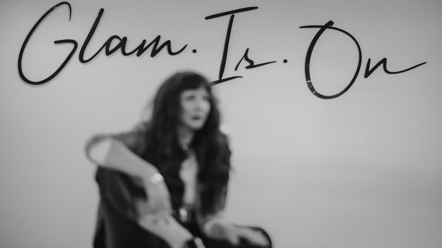 A woman is standing in front of a sign that says glam is on