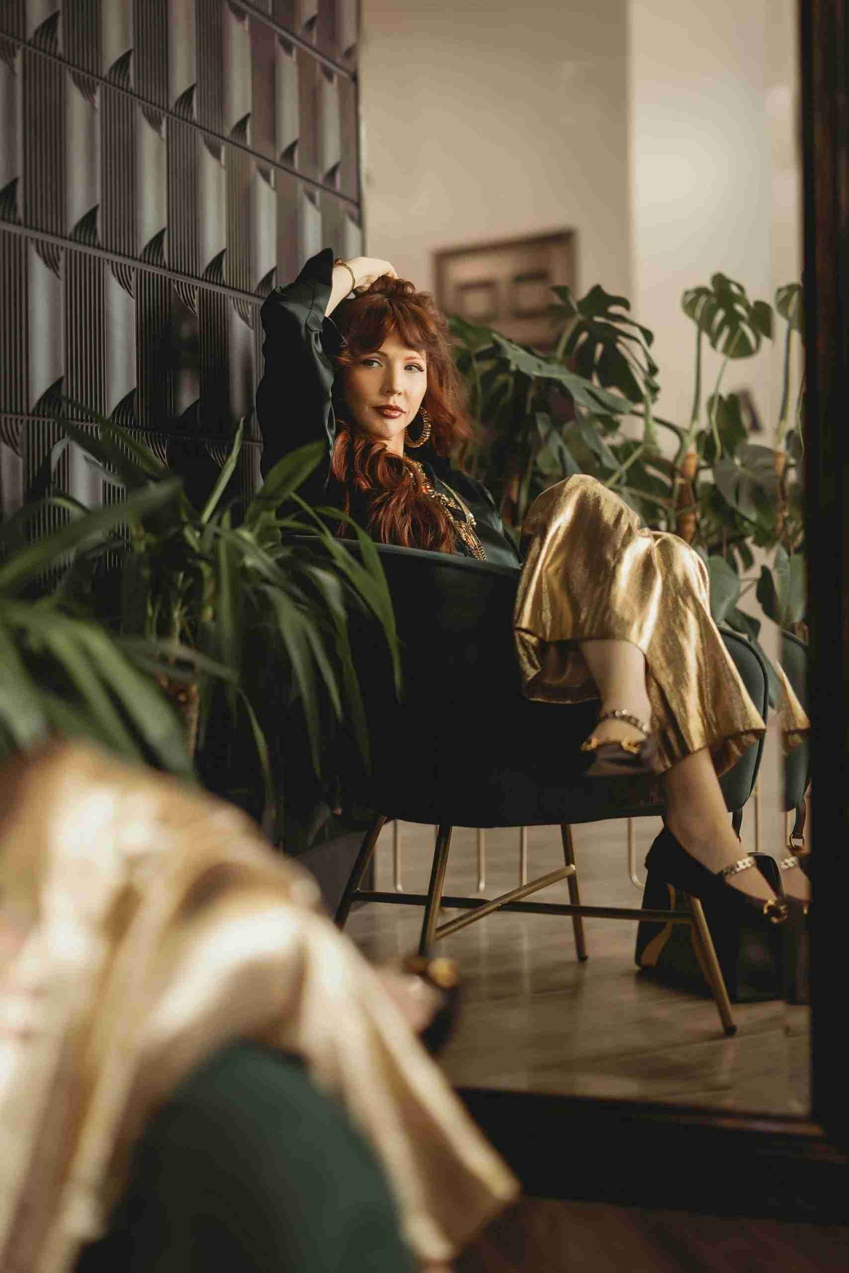A woman is sitting in a chair in front of a mirror surrounded by plants.