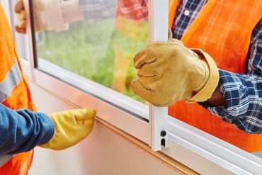 A Man Wearing Yellow Gloves Is Installing a Window — Distinctive Glass & Aluminium in Port Kembla, NSW