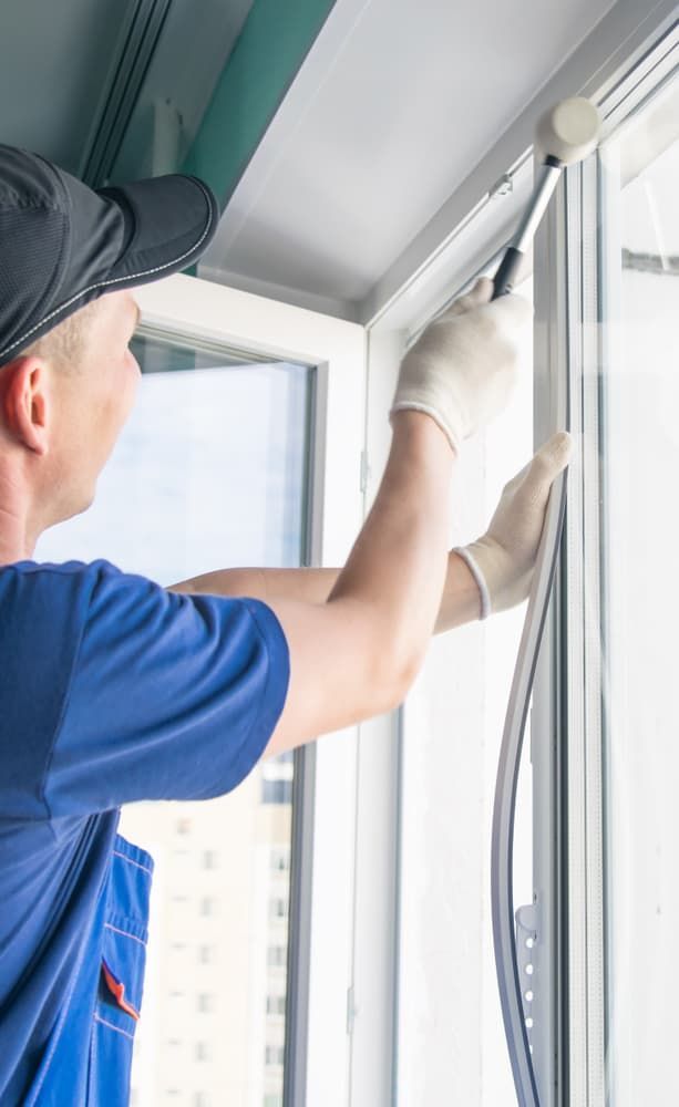 A Man Is Installing a Window in A House — Distinctive Glass & Aluminium in Thirroul, NSW