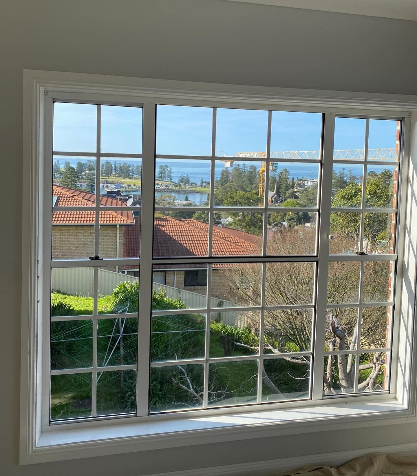 A white panelled window overlooking a house and the ocean  — Distinctive Glass & Aluminium in Port Kembla, NSW