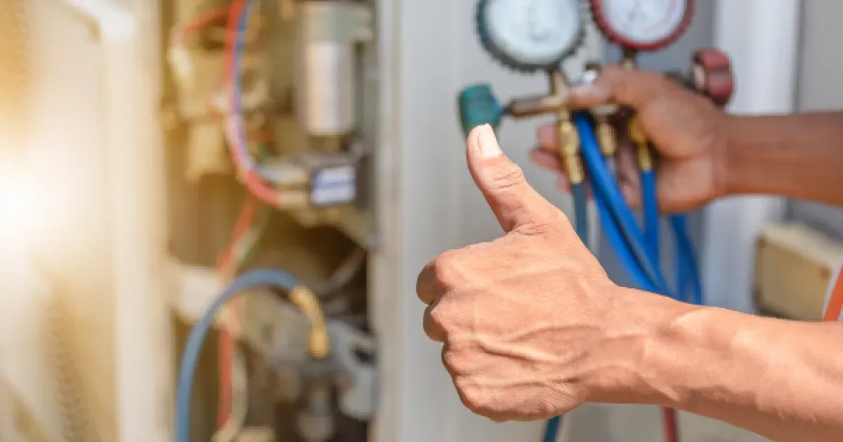 HVAC technician holding gauges, giving a thumbs up. Repairing a machine outdoors.