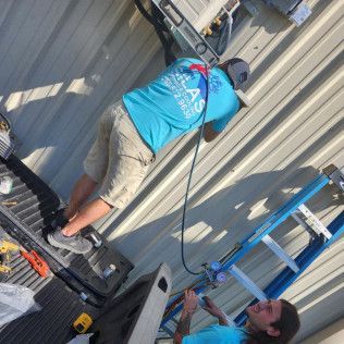 Two men working on a metal building. One on the roof, the other on a ladder. Tools are present.