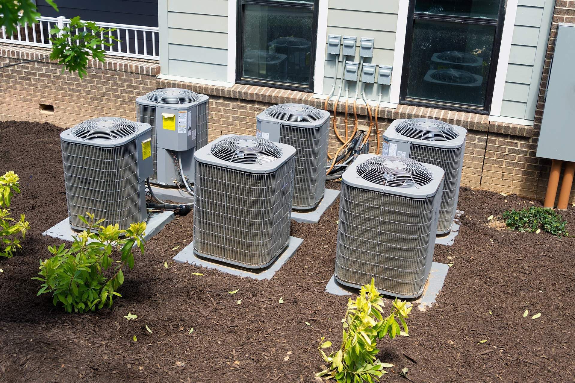 Six air conditioning units on concrete pads in a landscaped yard.