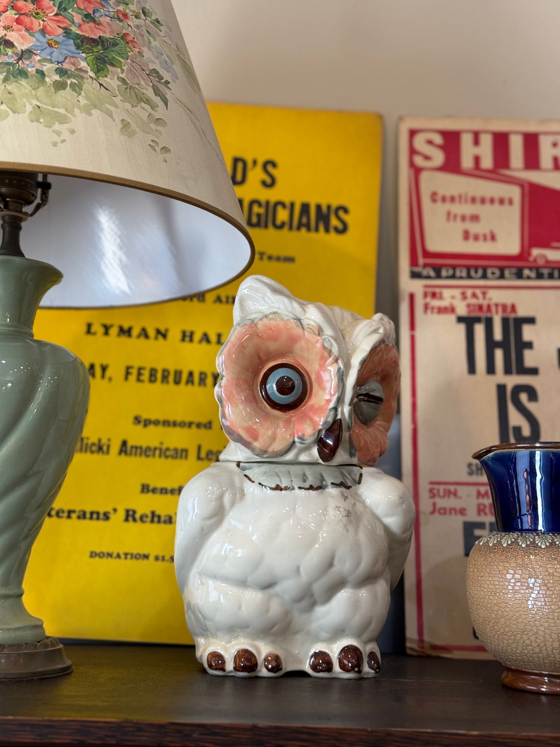 Ceramic owl figurine with a vintage lamp, books, and other decorative items.