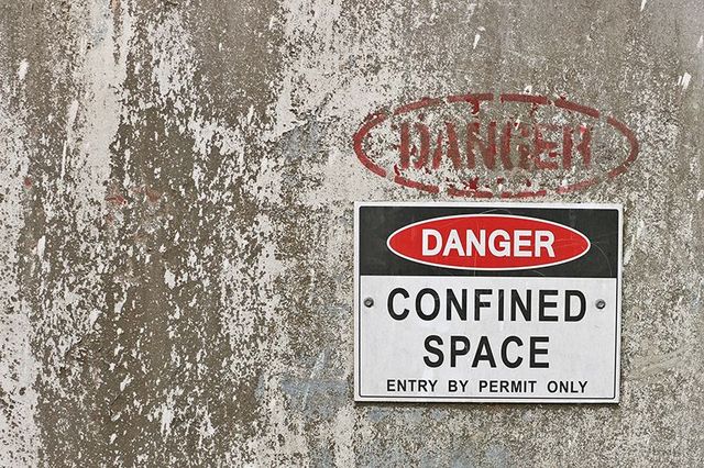 Danger sign on a concrete wall reading Confined space, entry by permit only