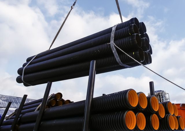 Crane sling lifting a bundle of black pipes