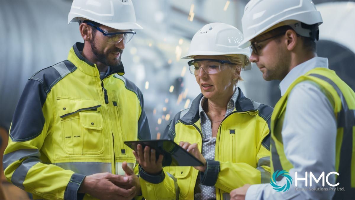 Three workers in hard hats and high-vis reviewing a tablet on site