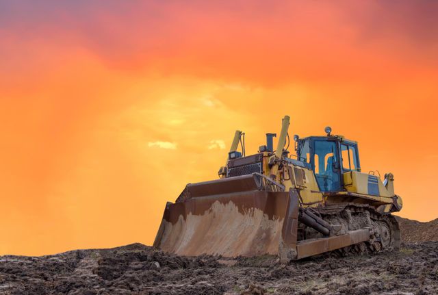 Bulldozer silhouetted against an orange sunset