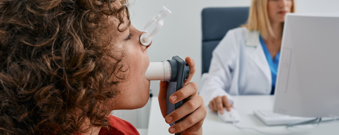 Person blowing into a spirometer while a clinician monitors the results