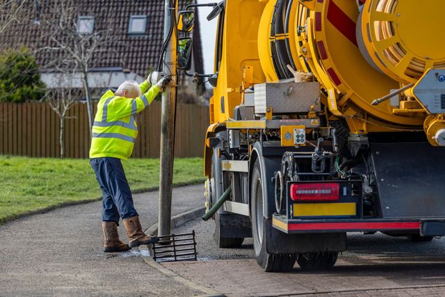 Worker in high-vis operating a vacuum truck on a residential street
