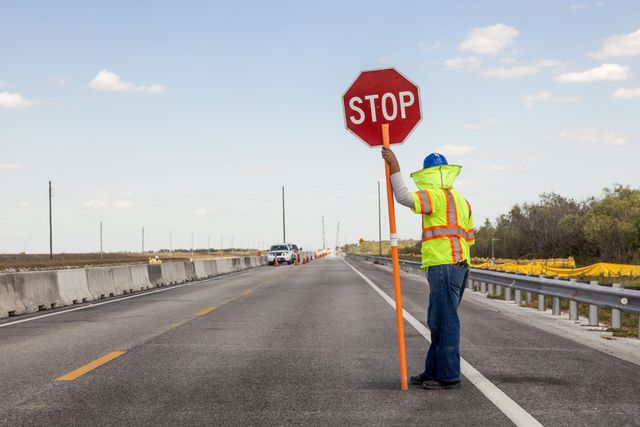 Traffic controller holding a stop sign on a road