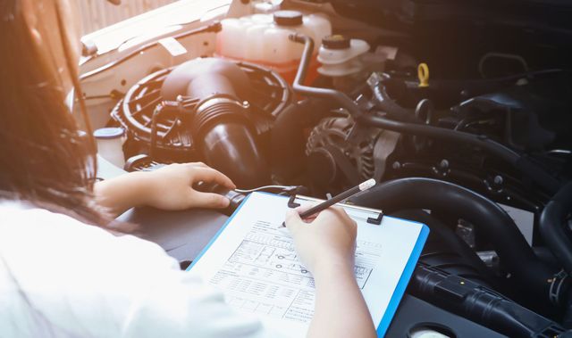 Person completing a vehicle inspection checklist over an open engine bay