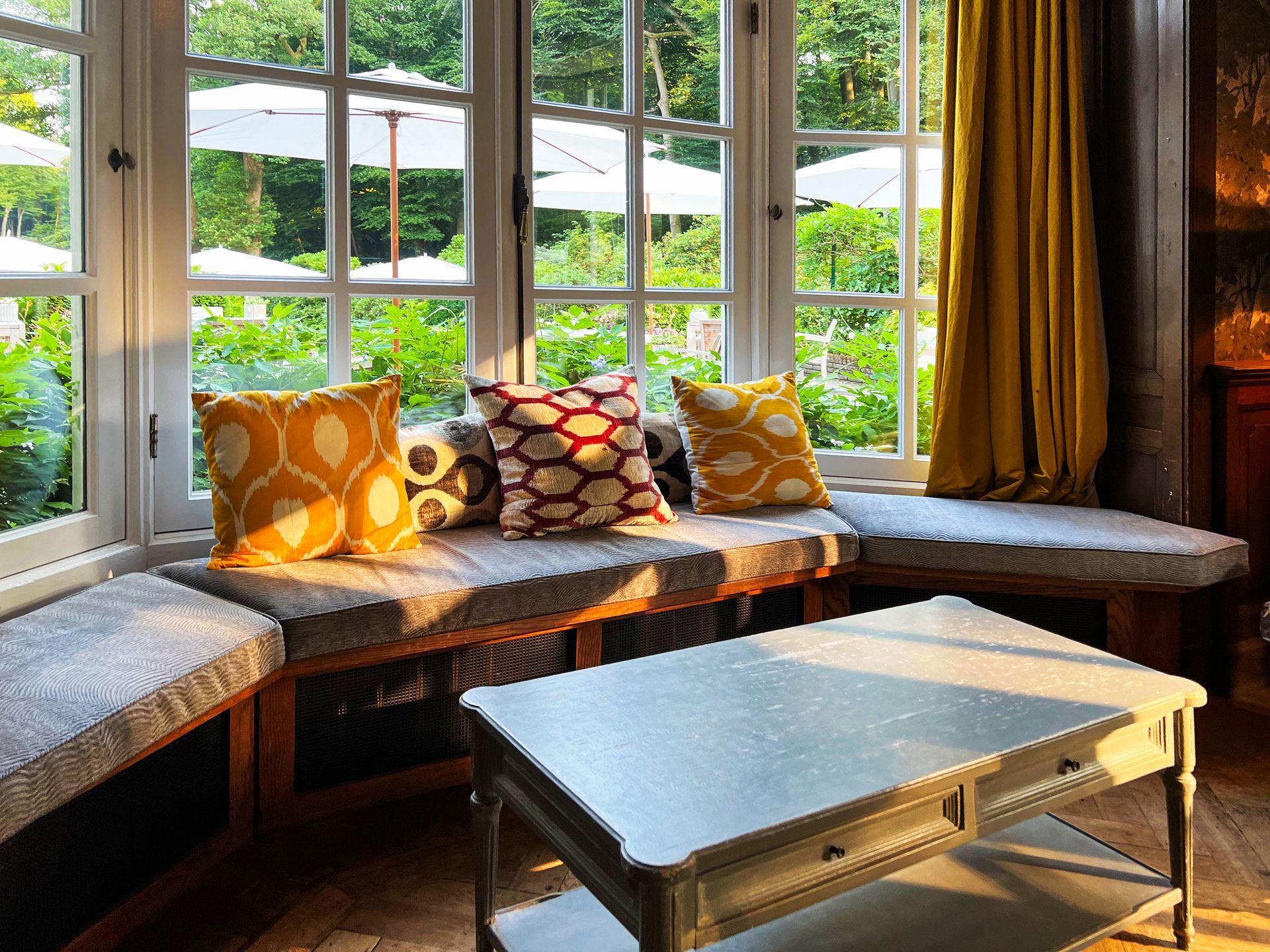 A bay window nook with comfy cushions and pillows, but in need of window treatments