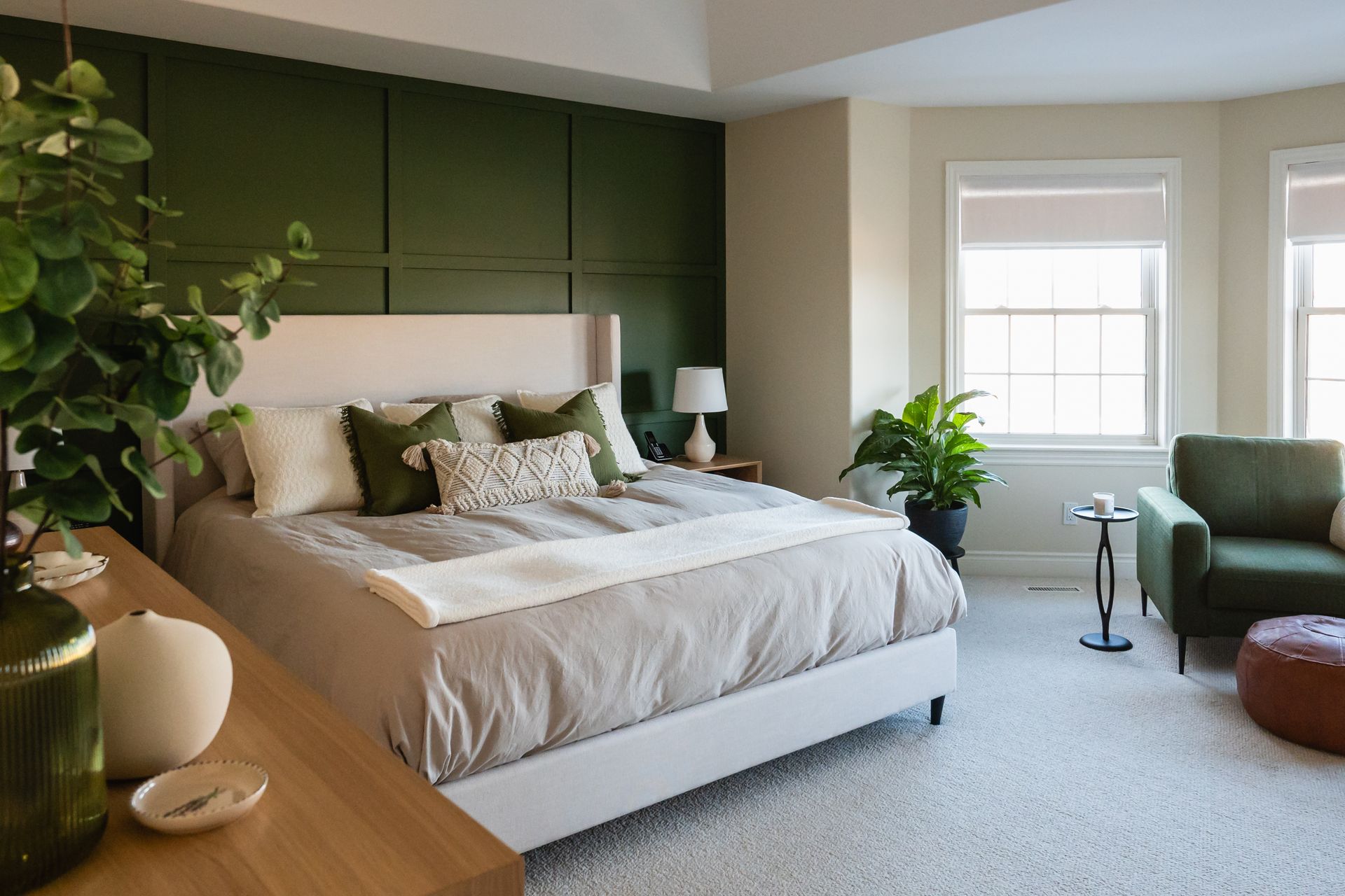 A cozy bedroom with a green accent wall and open roller shades at the window