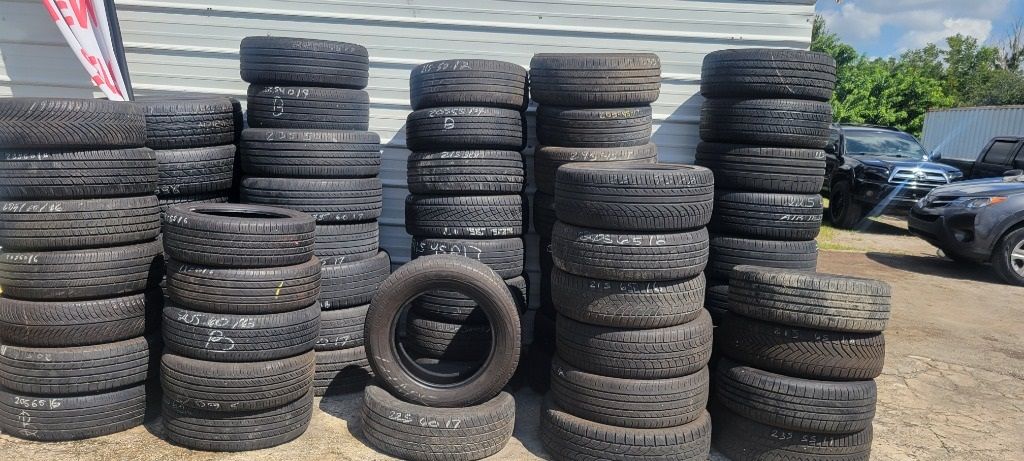 A bunch of tires are stacked on top of each other in a parking lot under the sun.