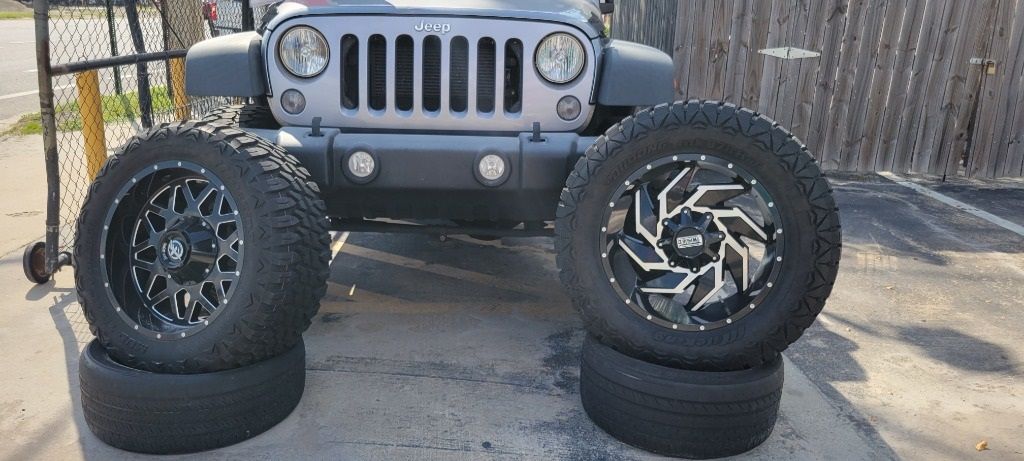 A jeep is parked next to a pile of tires and wheels.
