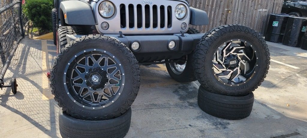 A jeep is parked next to a pile of new tires and wheels.