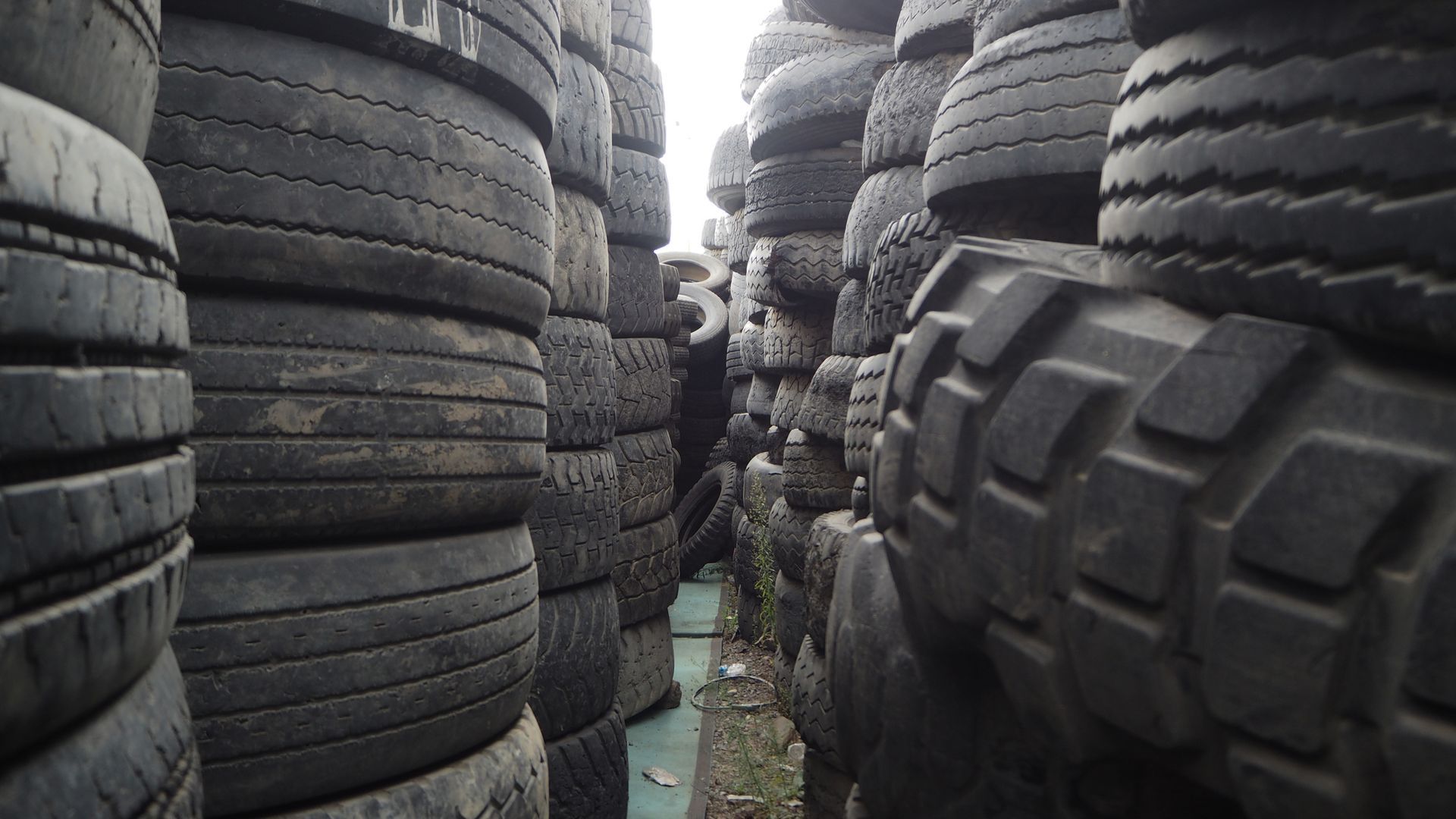 A bunch of used quality tires are stacked on top of each other on the field.