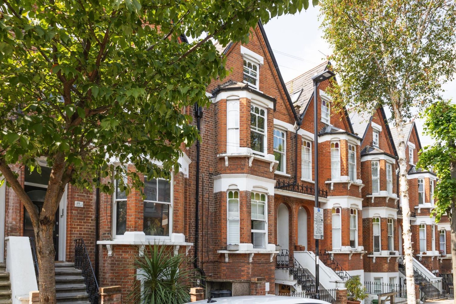 Snow-dusted red-brick row houses with white trim beneath leafy trees on a residential street