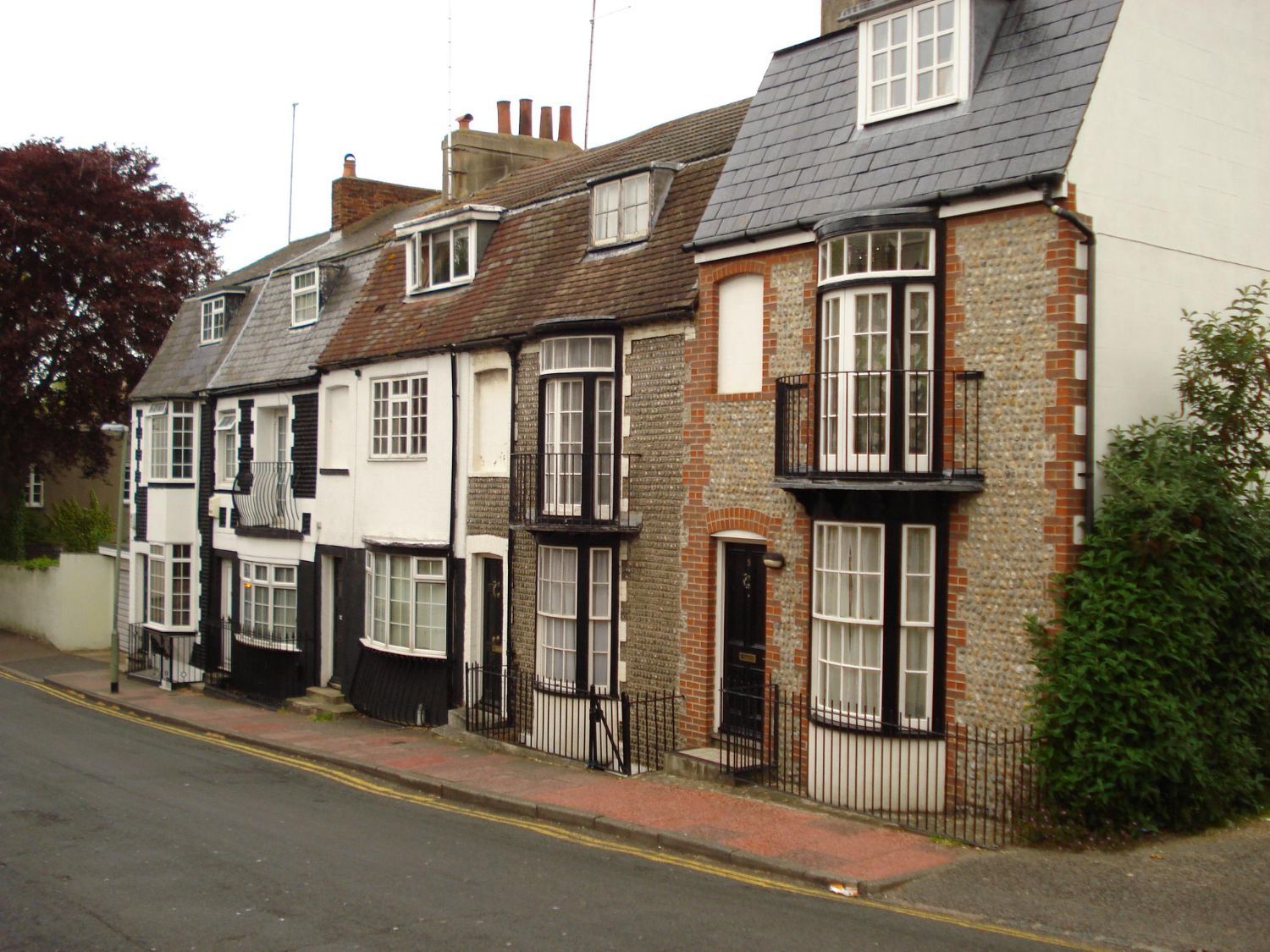 Row of old brick and white terraced houses on a quiet street under overcast skies