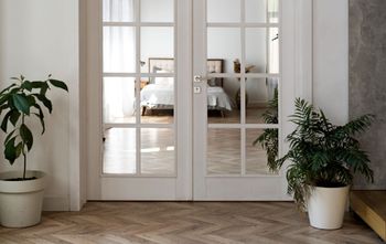 Bright hallway with white French doors, potted plants, and a glimpse into a sunlit bedroom