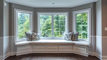 Built-in bay window seat with cushions and pillows in a bright room overlooking trees