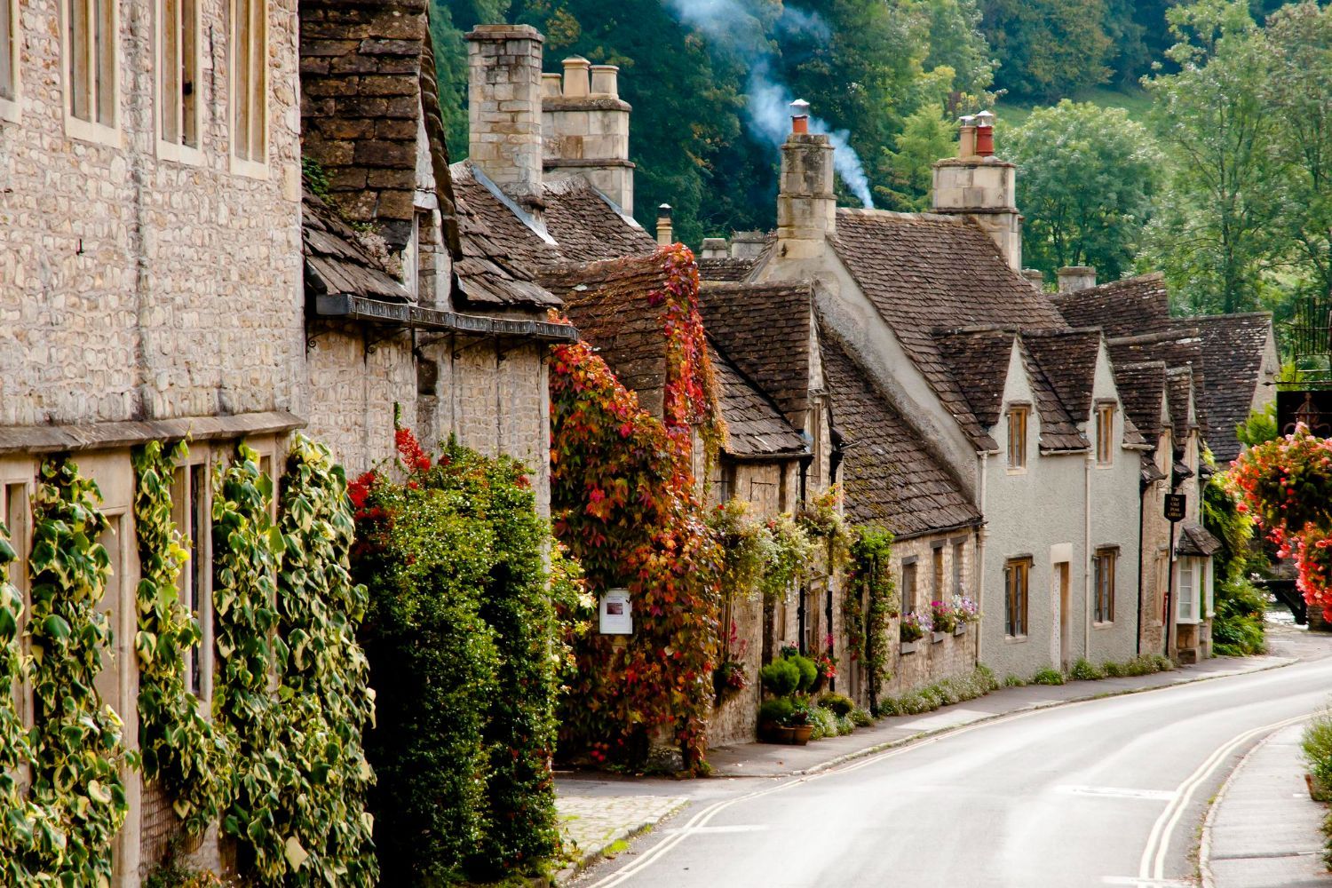 Quaint stone cottages lining a winding village road with ivy and colorful flowers