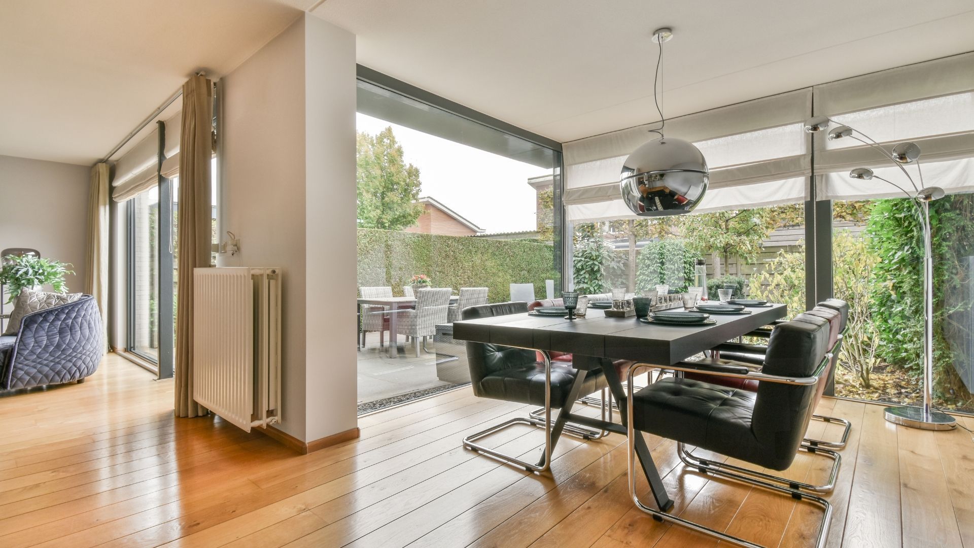 Modern dining area with glass table, black chairs, pendant light, and open view to a patio and garden