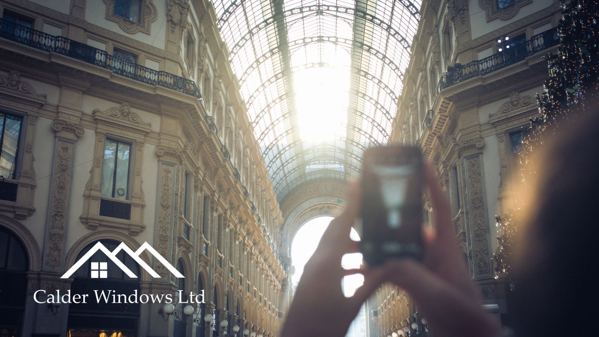 Hands holding a phone to photograph a grand indoor hall with a glass ceiling and ornate architecture