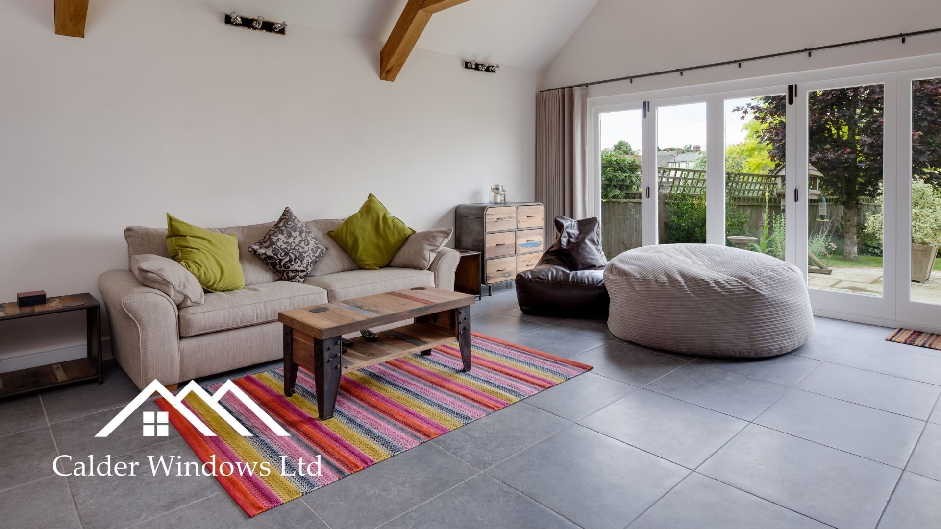 Bright living room with sofa, colorful rug, bean bags, coffee table, and large glass doors to a garden