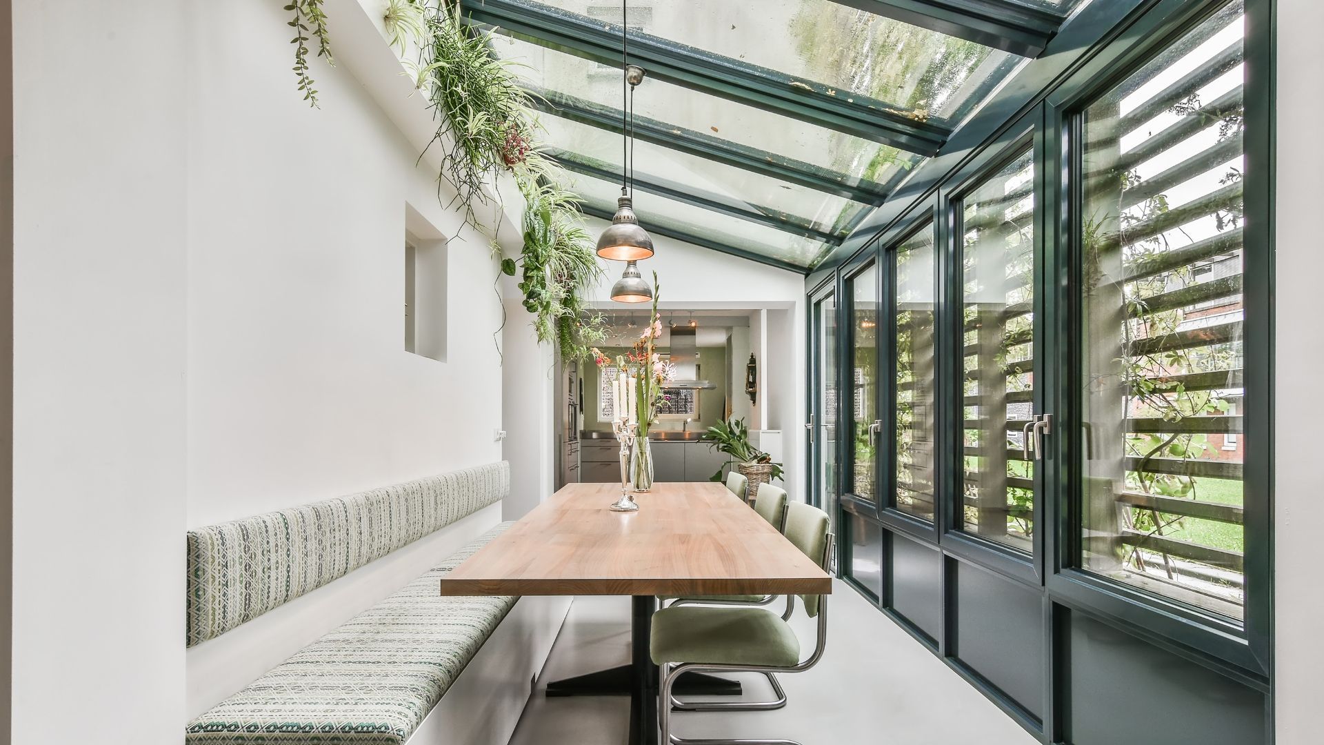 Modern glass-roofed café corridor with wooden tables, bench seating, and hanging greenery