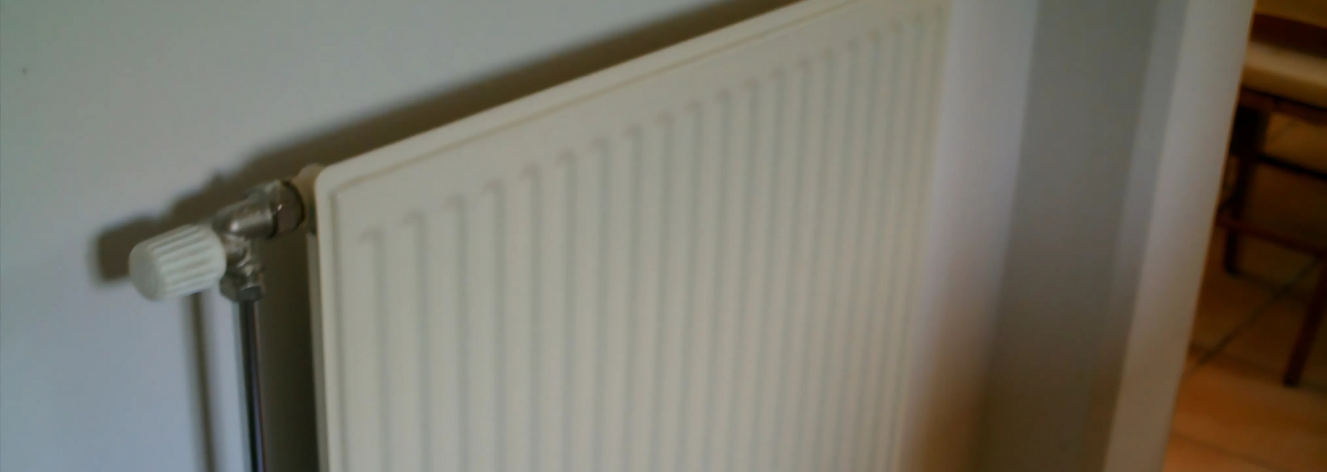 White radiator mounted on a wall beside a doorway in a room with light-colored walls.