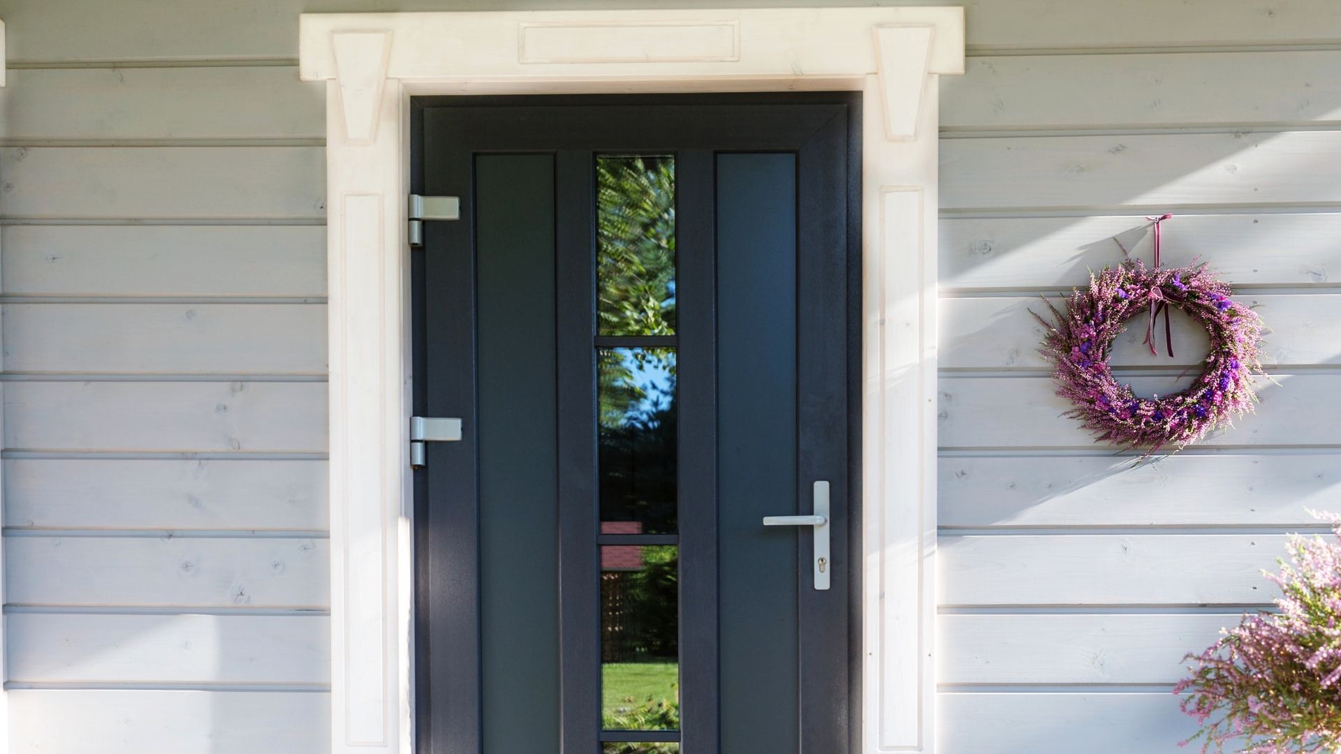 Front door with gray siding, white trim, and a pink wreath hanging on the wall.