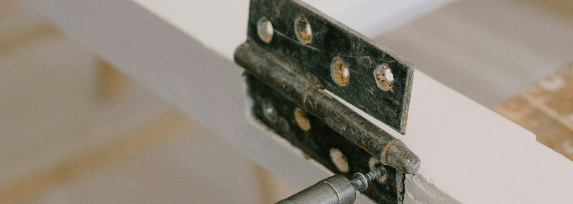 Close-up of a metal hinge connecting two white wooden slats against a beige background